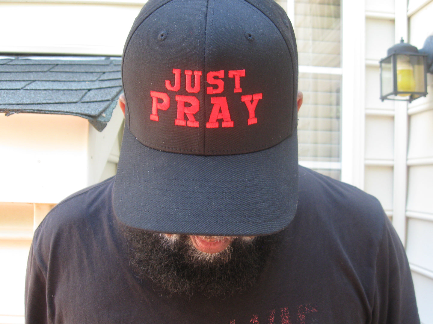 A structured, six-panel twill cap in a black color featuring the words "Just Pray" embroidered on the front. The cap has a low-profile embroidery area, six vent eyelets for breathability. It is displayed on a neutral background.