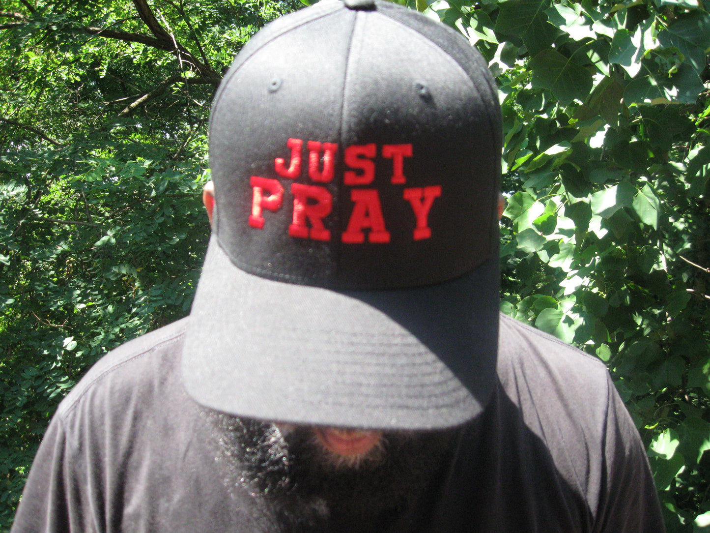 A structured, six-panel twill cap in a black color featuring the words "Just Pray" embroidered on the front. The cap has a low-profile embroidery area, six vent eyelets for breathability. It is displayed on a neutral background.