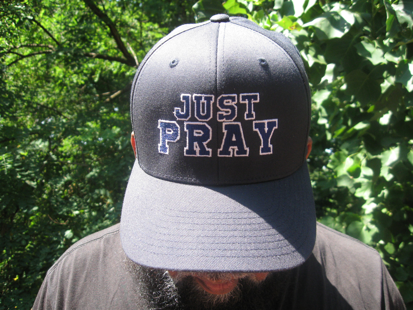 A structured, six-panel twill cap in a blue color featuring the words "Just Pray" embroidered on the front. The cap has a low-profile embroidery area, six vent eyelets for breathability. It is displayed on a neutral background.