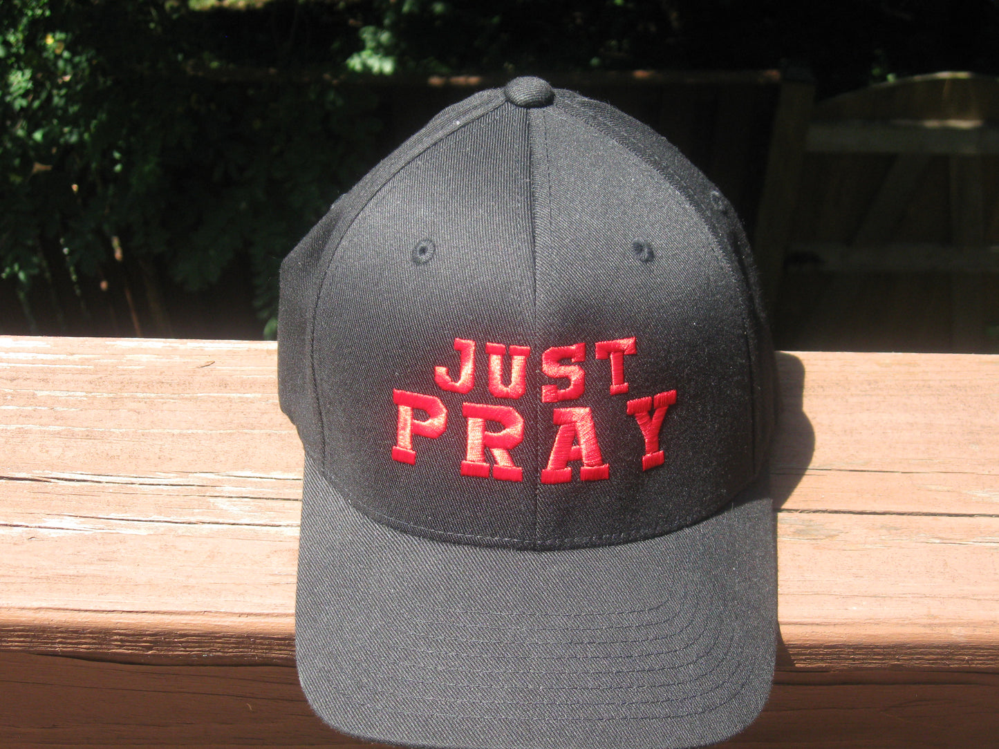 A structured, six-panel twill cap in a black featuring the words "Just Pray" embroidered on the front. The cap has a low-profile embroidery area, six vent eyelets for breathability. It is displayed on a neutral background.