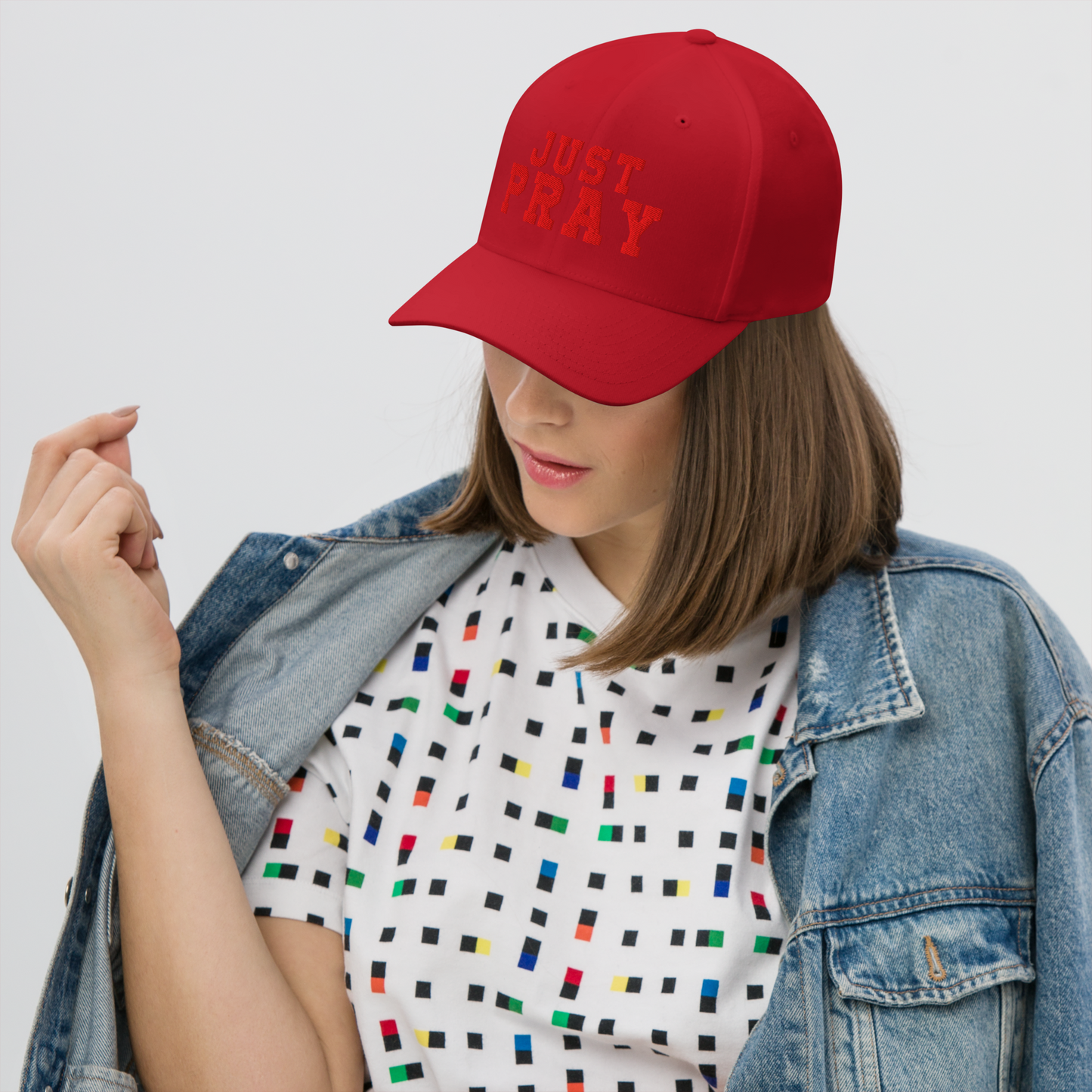 A structured, six-panel twill cap in a red color featuring the words "Just Pray" embroidered on the front. The cap has a low-profile embroidery area, six vent eyelets for breathability. It is displayed on a neutral background.