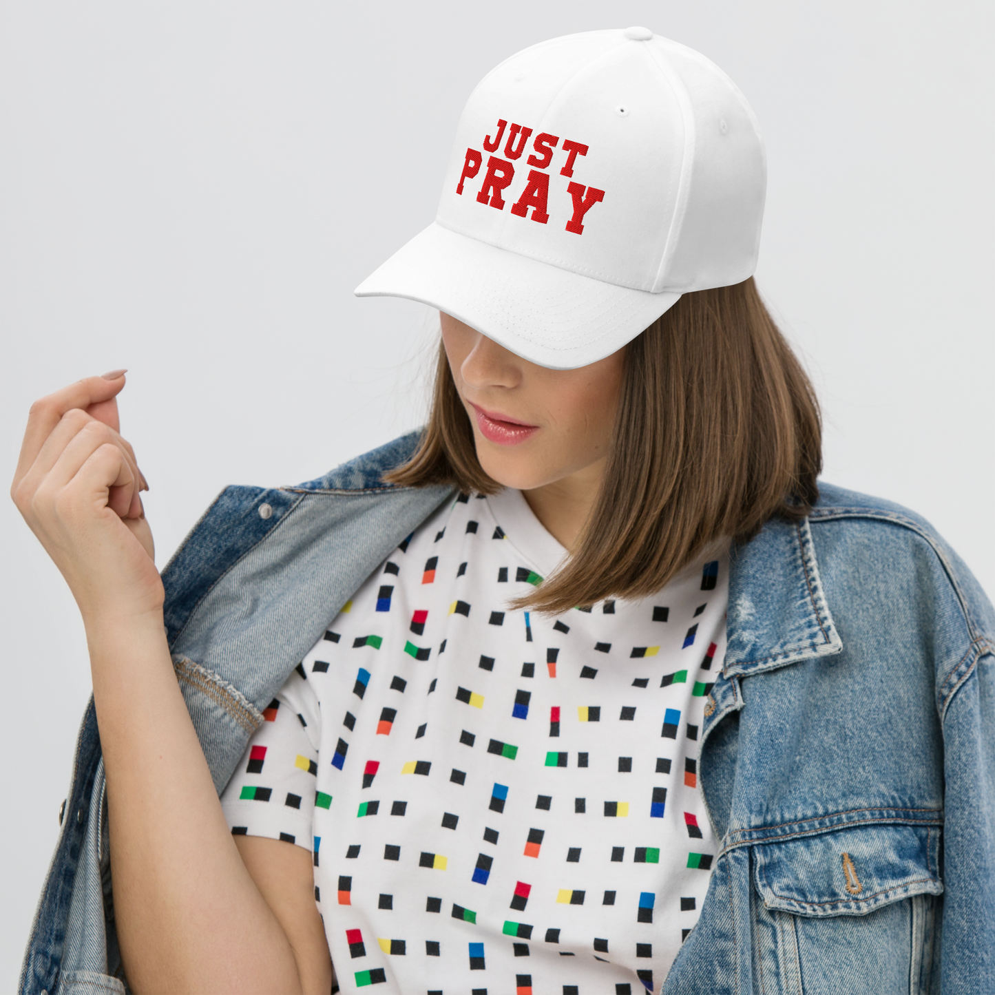 YesA structured, six-panel twill cap in a white color featuring the words "Just Pray" embroidered on the front. The cap has a low-profile embroidery area, six vent eyelets for breathability. It is displayed on a neutral background.
