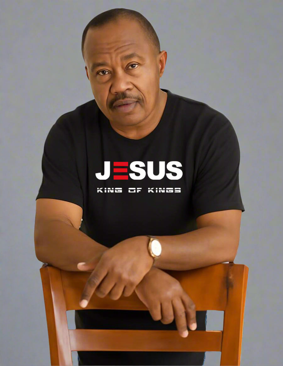 Man wearing a black t-shirt with 'Jesus King of Kings' text, sitting on a wooden chair.