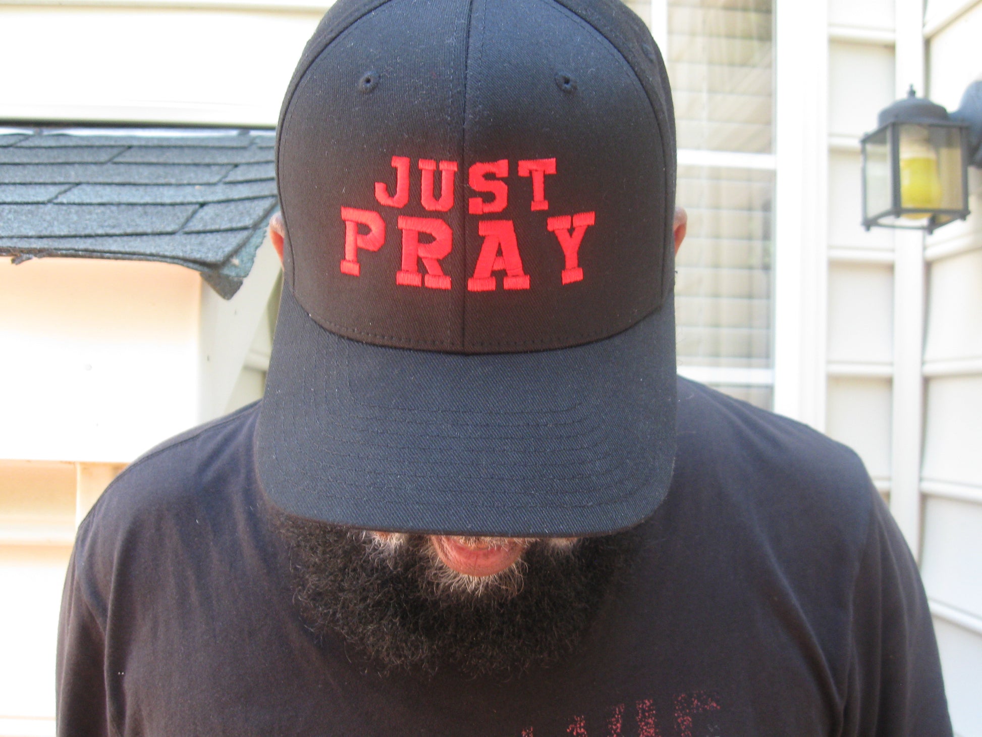 A structured, six-panel twill cap in a black color featuring the words "Just Pray" embroidered on the front. The cap has a low-profile embroidery area, six vent eyelets for breathability. It is displayed on a neutral background.